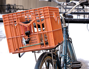 This person secured a milk crate with bungee cable to their rear rack for extra storage. They have a coffee cup in the basket, which is sure to tip over and be jumbled about during riding.