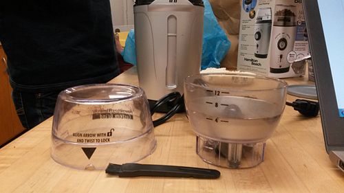 Top cover (left), back of coffee grinder (rear), cup with measurements (right), and brush (front)